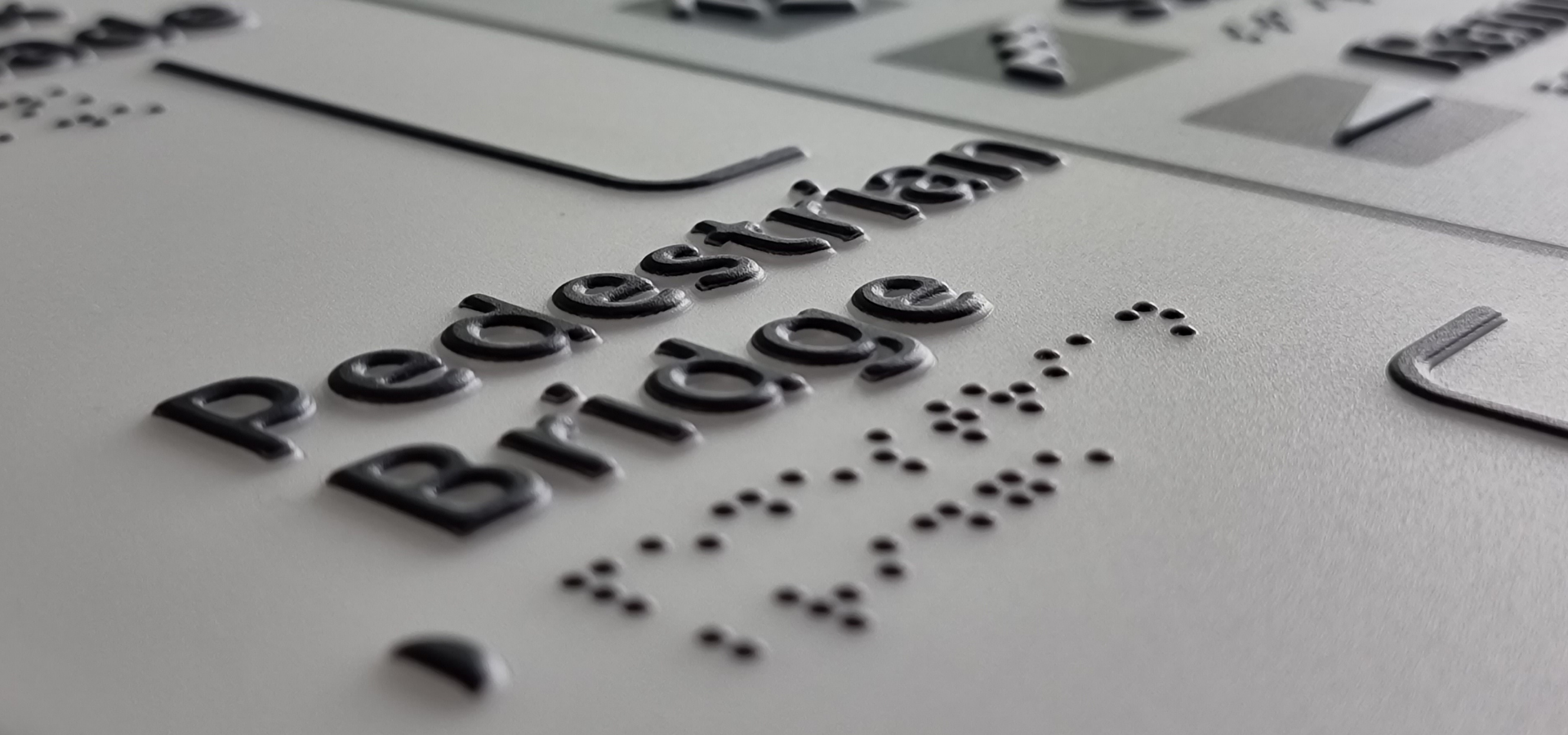 Braille text on a surface with 'Pedestrian Bridge' and braille characters.