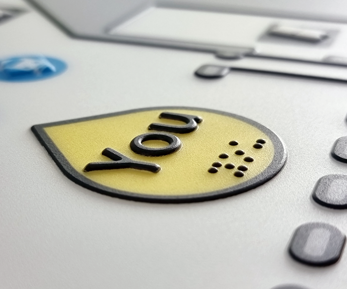 Close-up of a button labeled 'YOU' on a braille tactile map with braille text.