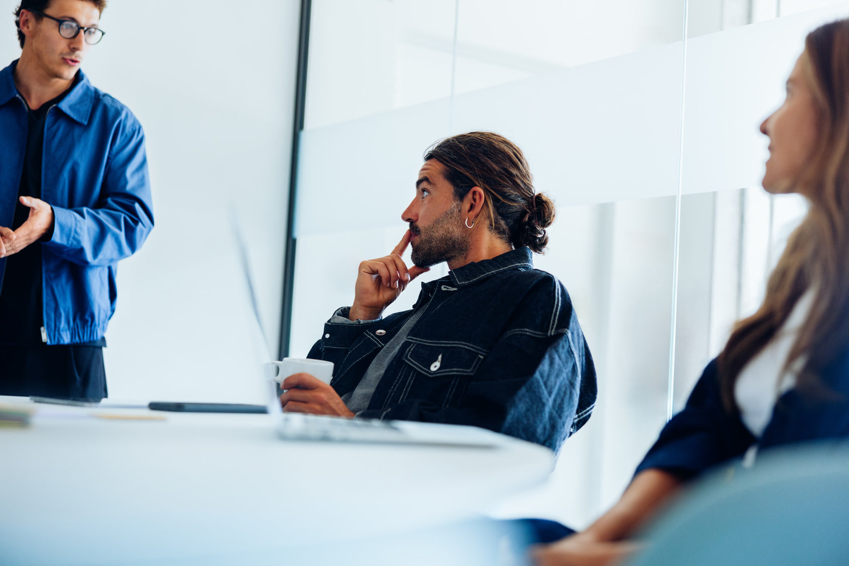 Three people in a meeting setting with one person using a laptop.
