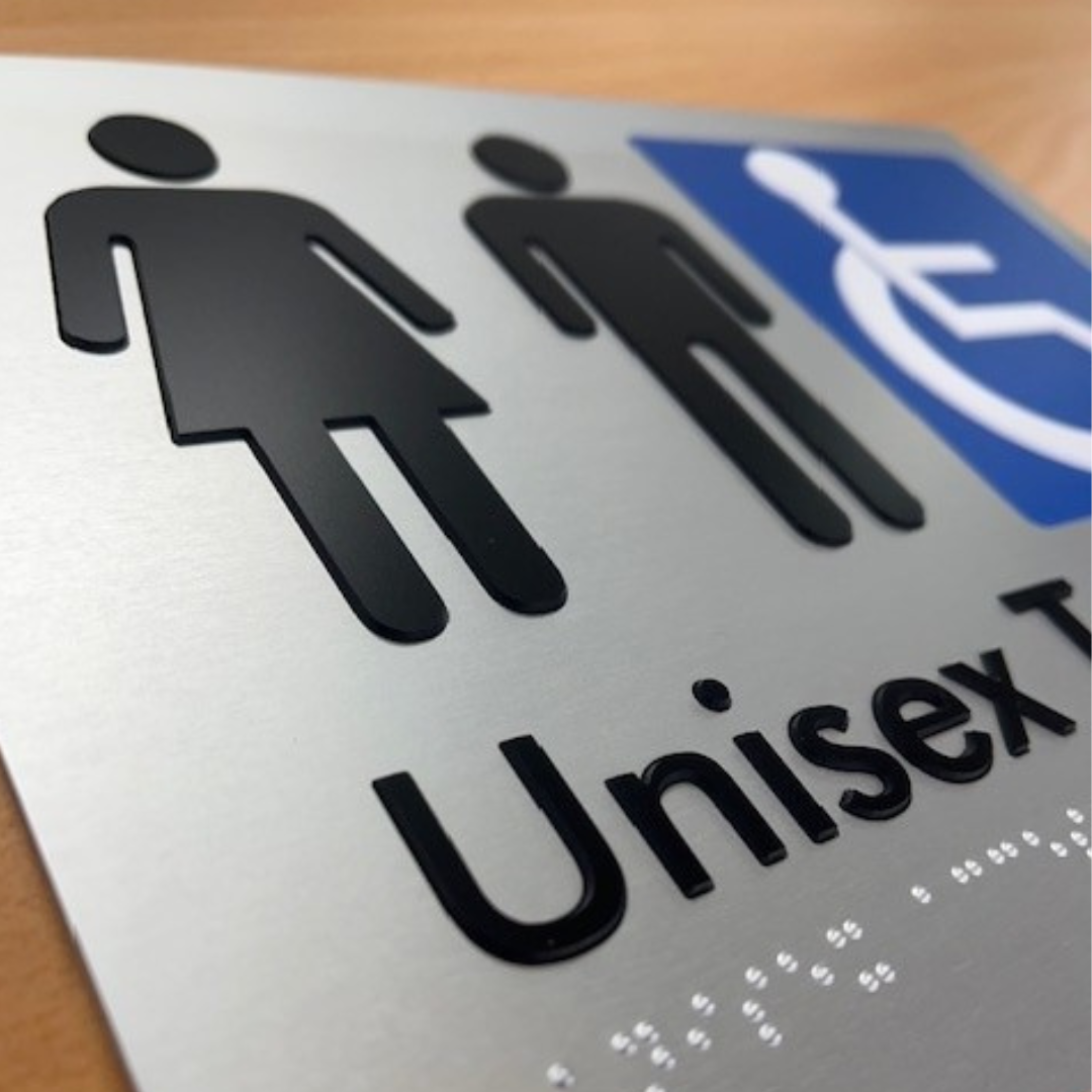 Unisex restroom braille tactile sign with blue accessibility symbol on a wooden surface