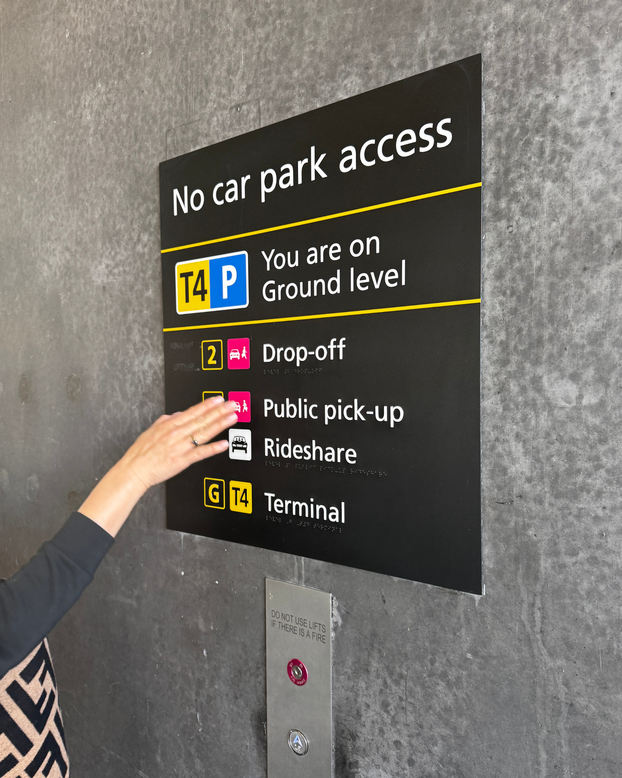Hand touching a braille sign with parking information on a gray wall.