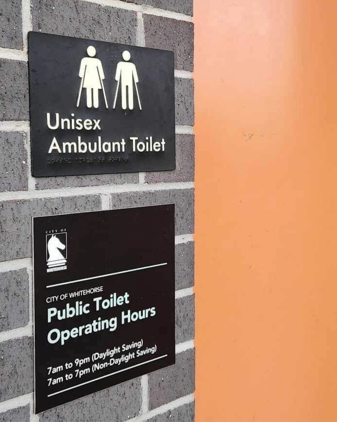 Unisex ambulant toilet braille sign on a brick wall with operating hours information braille sign.