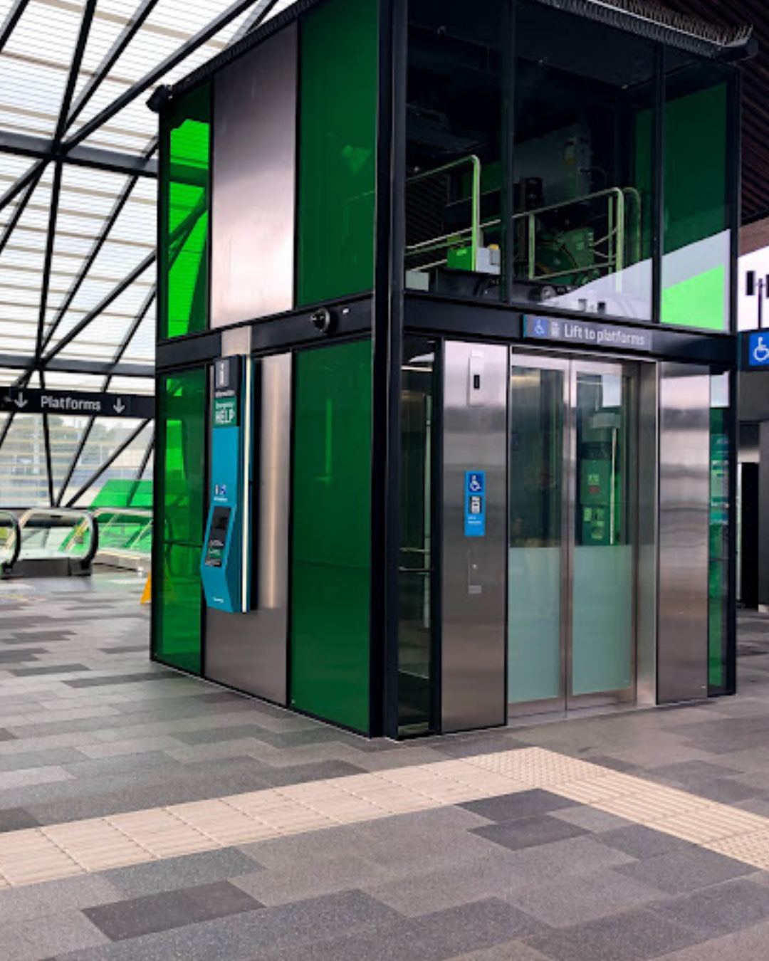 Modern train station platform with a green and silver automated ticket machine, and braille signage.