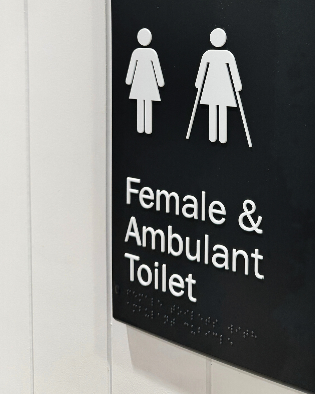 Compliant Braille Signage - Black sign with white symbols and text indicating a female and ambulant toilet.