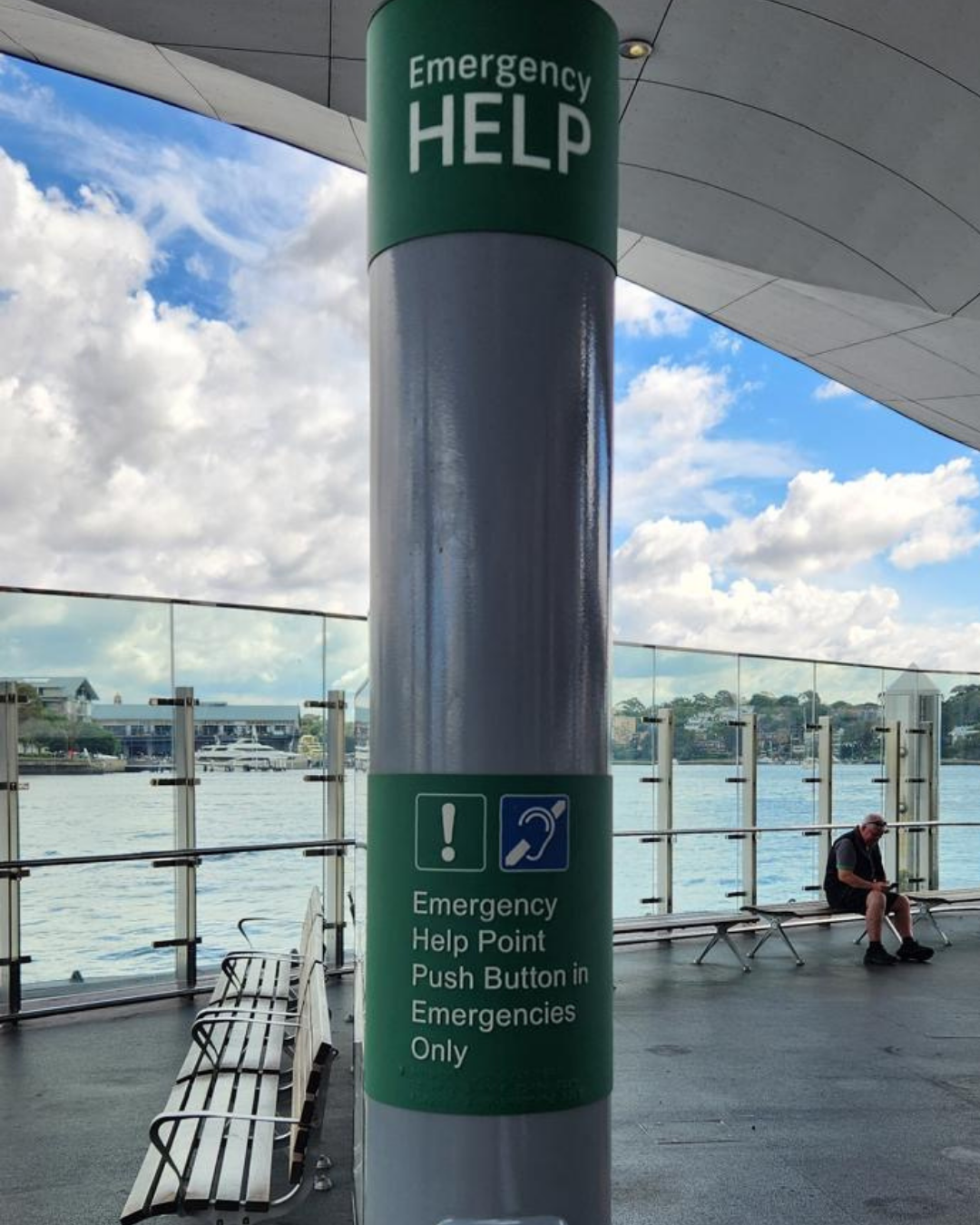 Emergency help sign with braille on a pillar, with a waterfront view in the background.