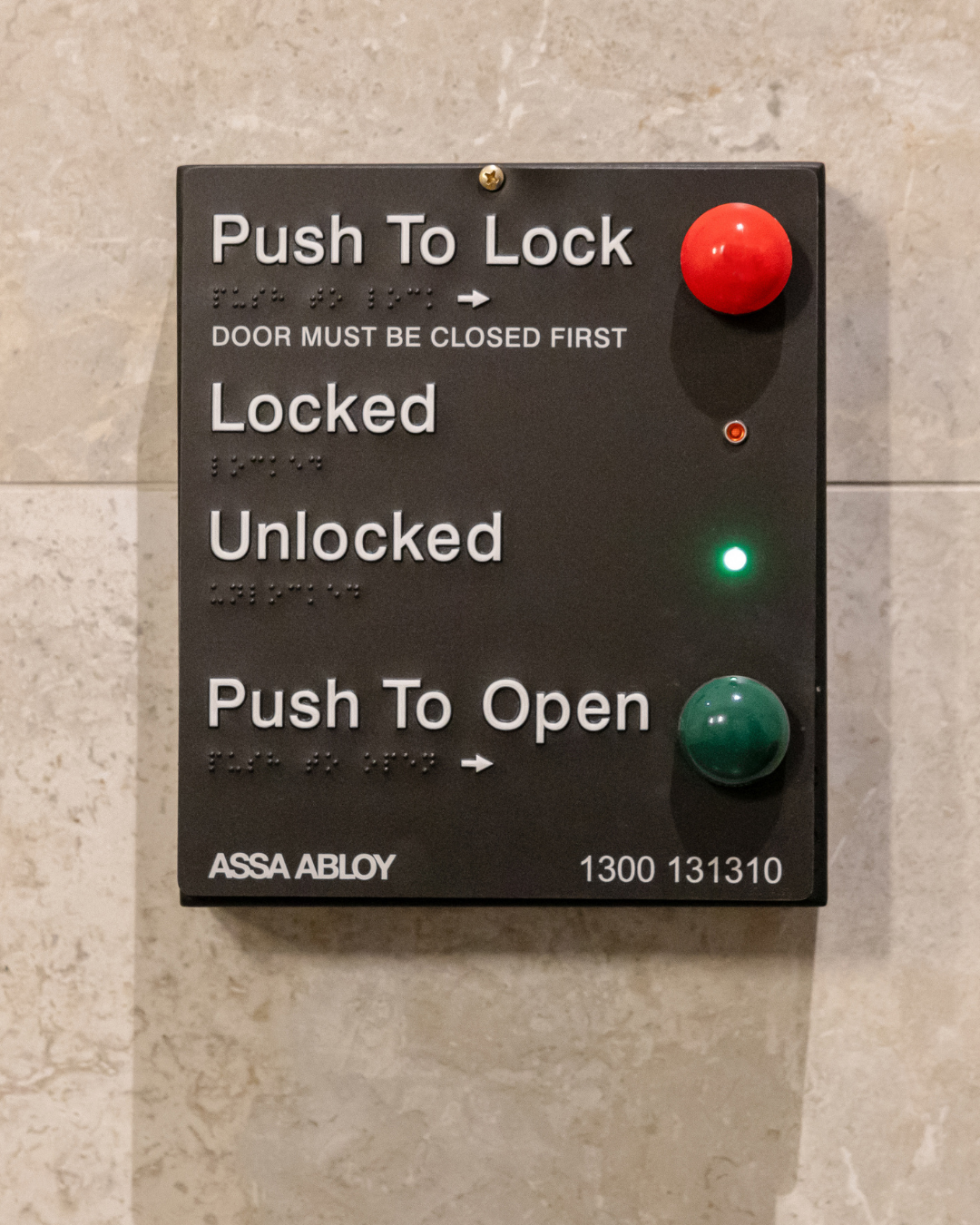 Door access control panel with push buttons, braille tactile elements and LED indicators on a tiled wall.