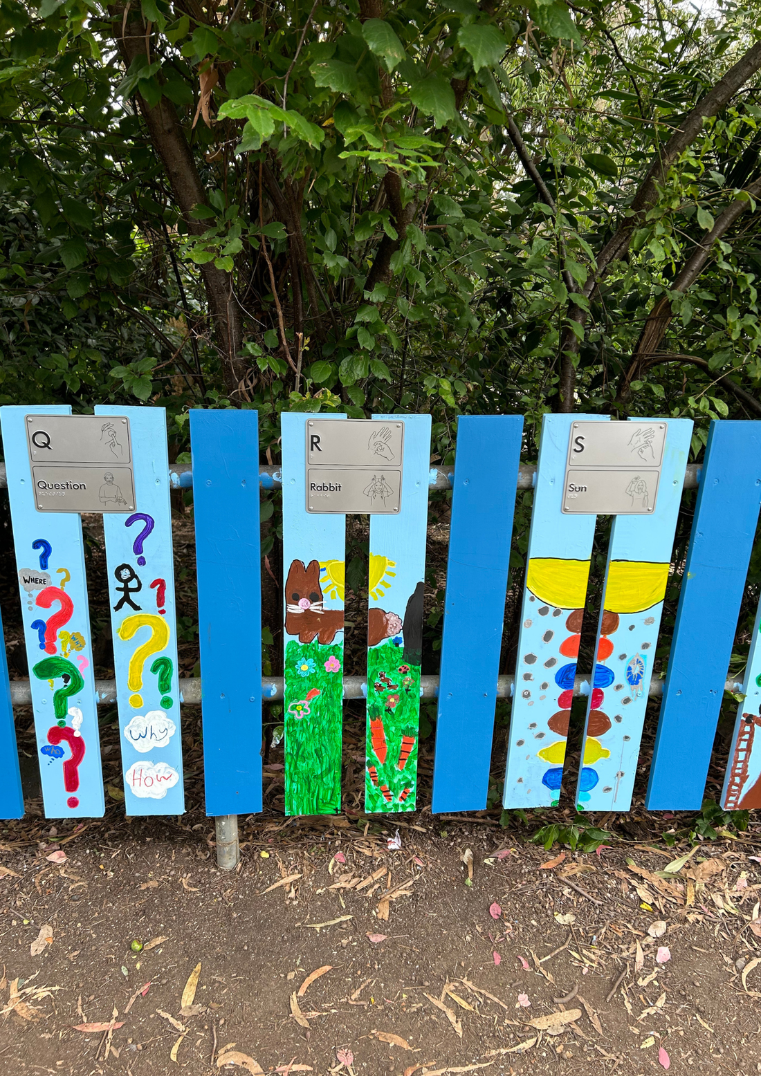 Colourfully paitned wooden fence with AUSLAN hand symbols braille signage, for the letters Q, R and S.