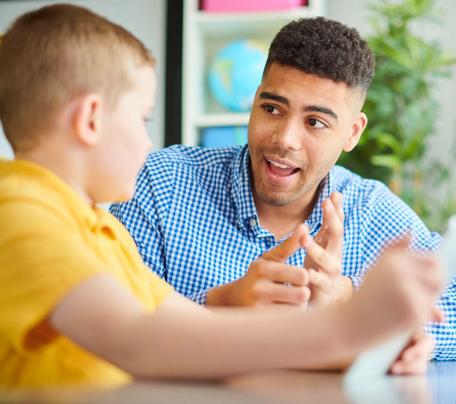 Man and child engaged in a conversation using sign language, at a table with a blurred background.