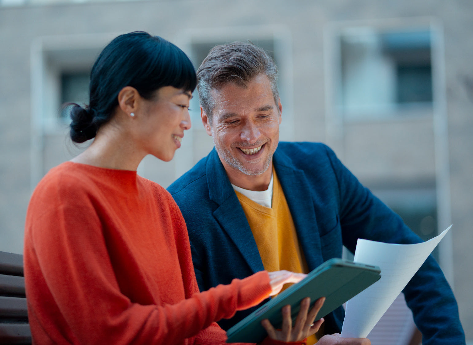 Two people looking at a tablet outdoors with a blurred background