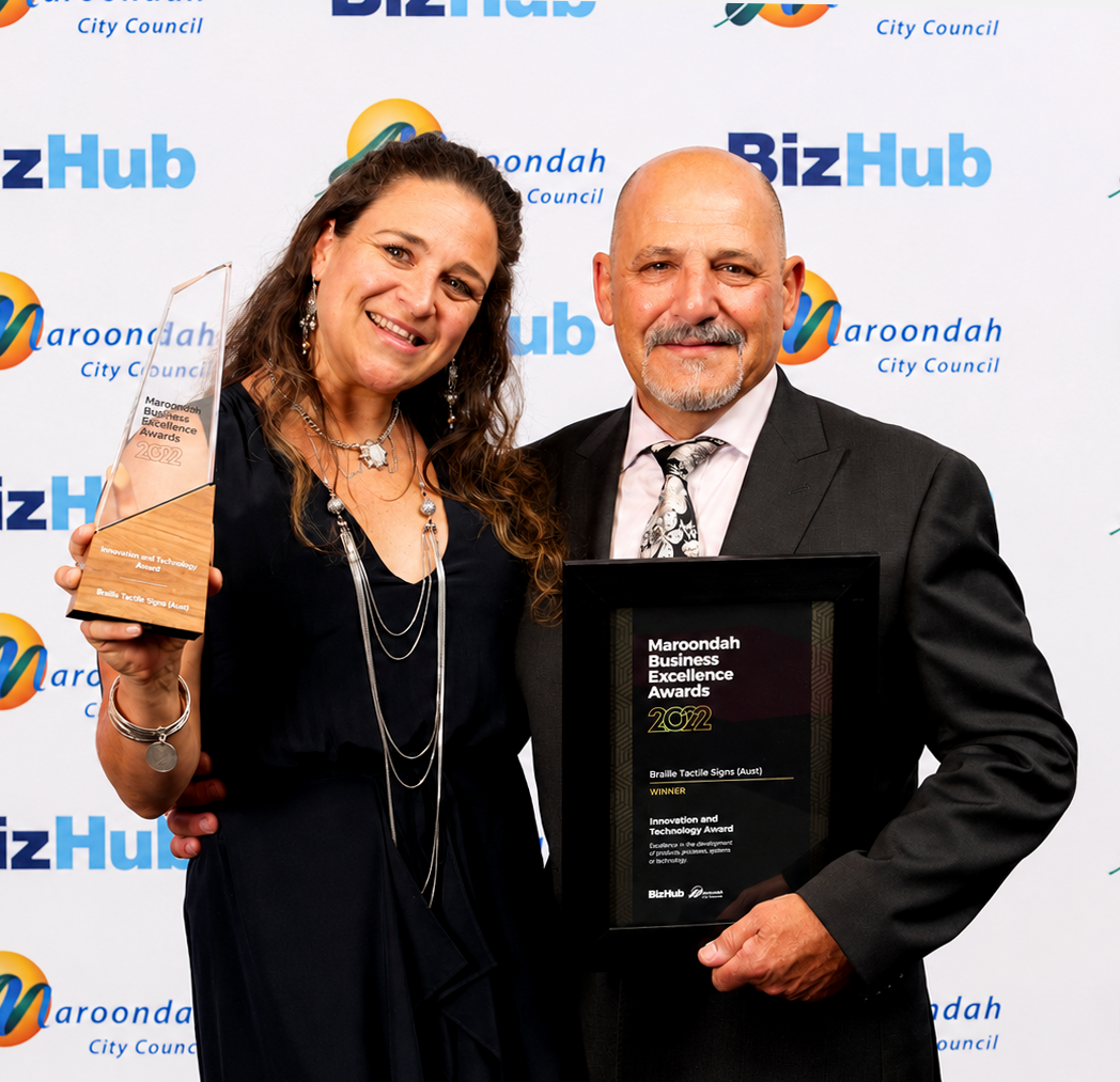Claudia and Roland Gatt, owners of Braille Tactile Signs Aust. in front of a BizHub and Maroondah City Council backdrop