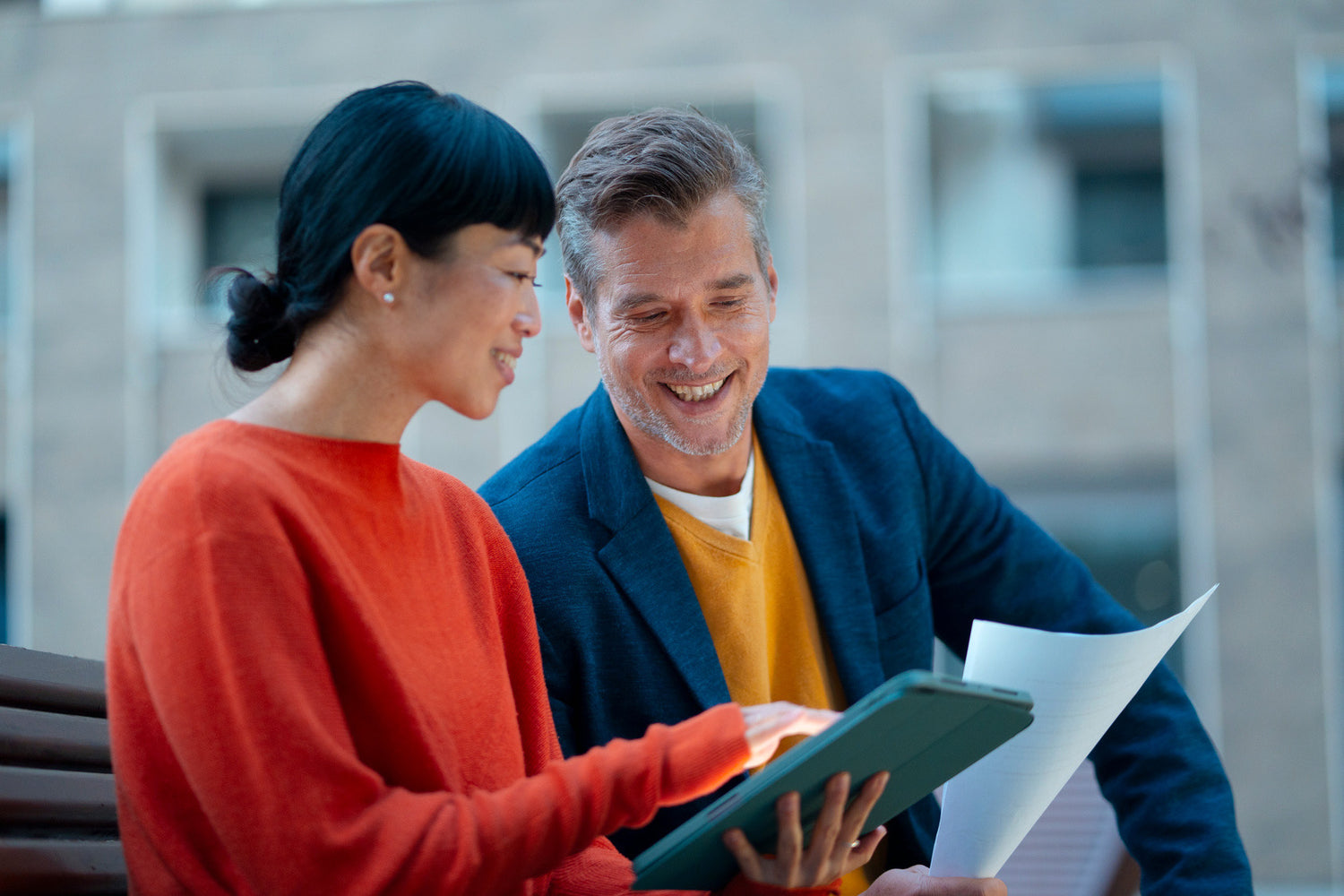 Two people looking at a tablet outdoors with a blurred background
