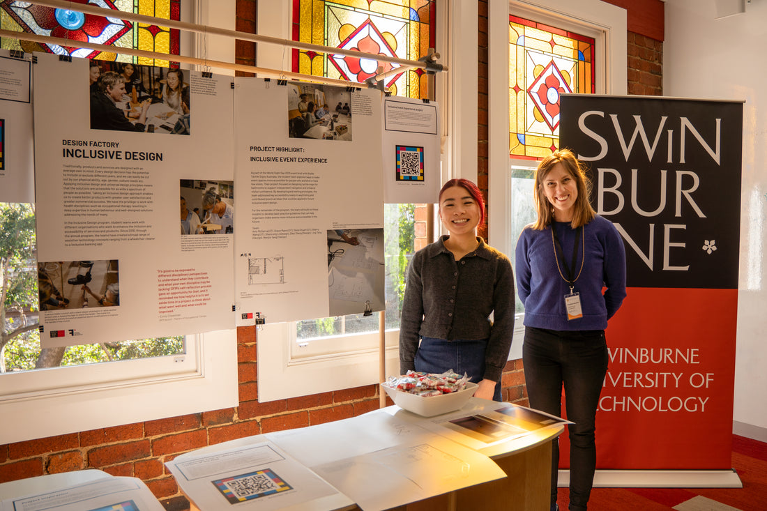 Two women standing in front of a 'Swinburne' sign with educational posters on a wall.