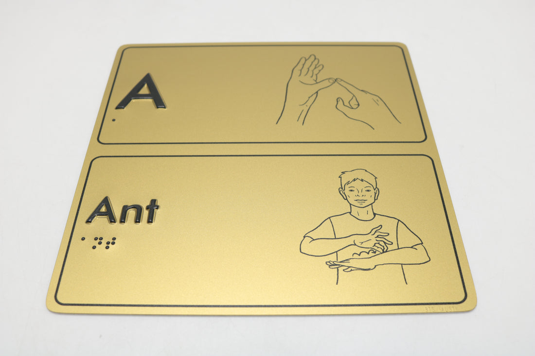 Gold sign with letter 'A' and AUSLAN hand gesture illustration on a white background, with braille elements.