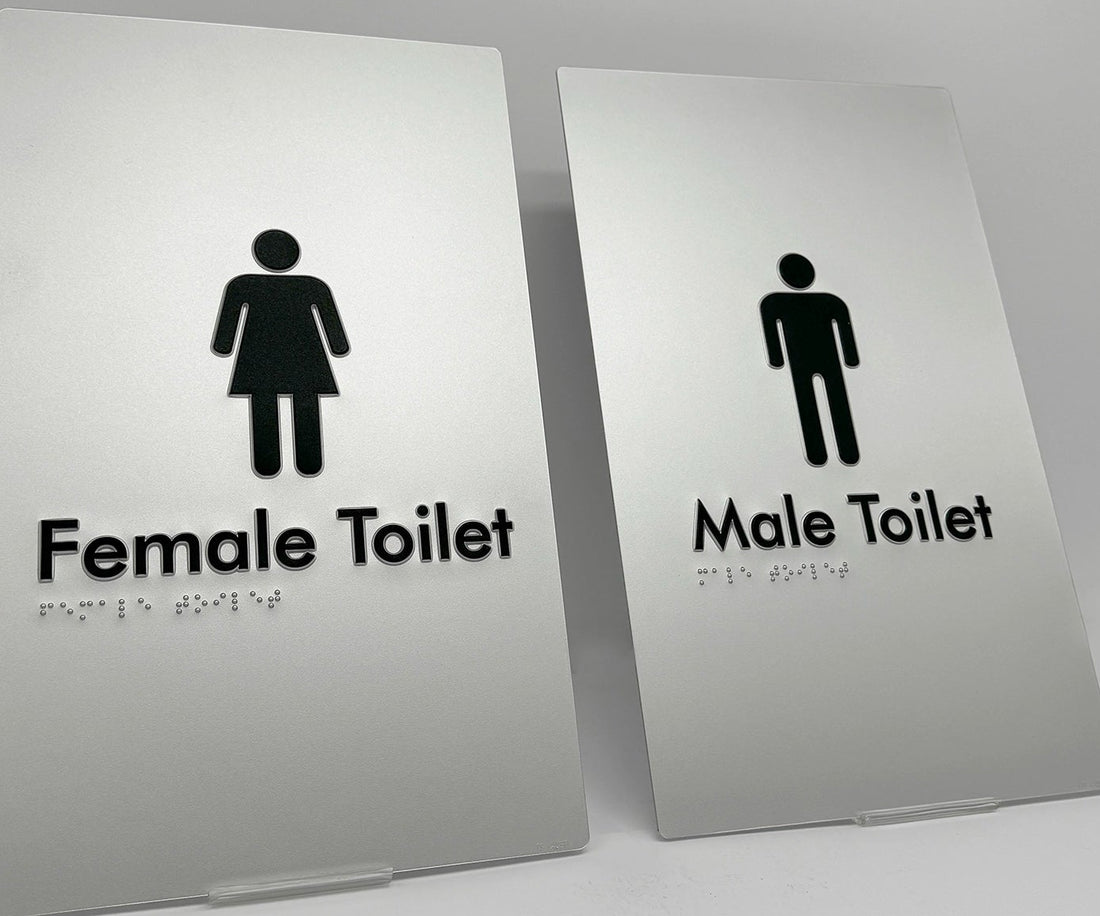 Two bathroom braille signs indicating 'Female Toilet' and 'Male Toilet'.