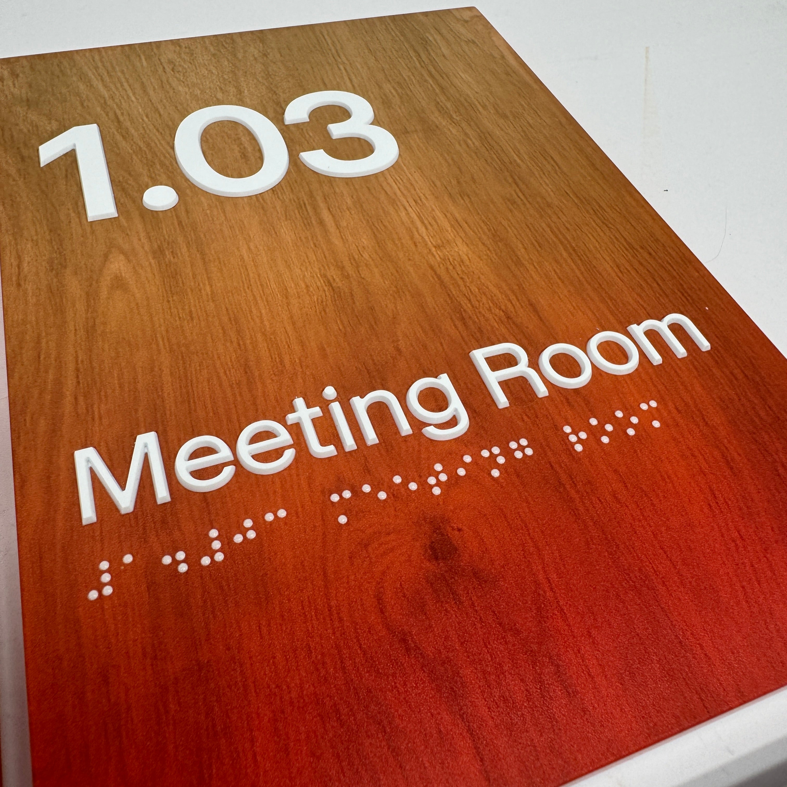 Wooden sign with '1.03 Meeting Room' text and braille for accessibility.