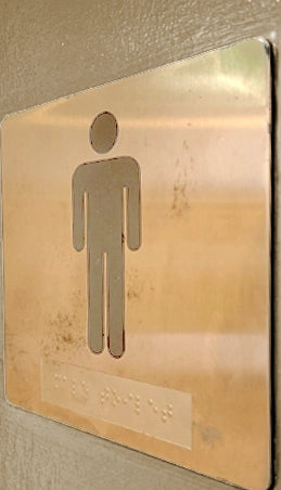 Non-compliant braille sign, as the metallic men's restroom sign has rusted and doesn't meet contrast requirements.