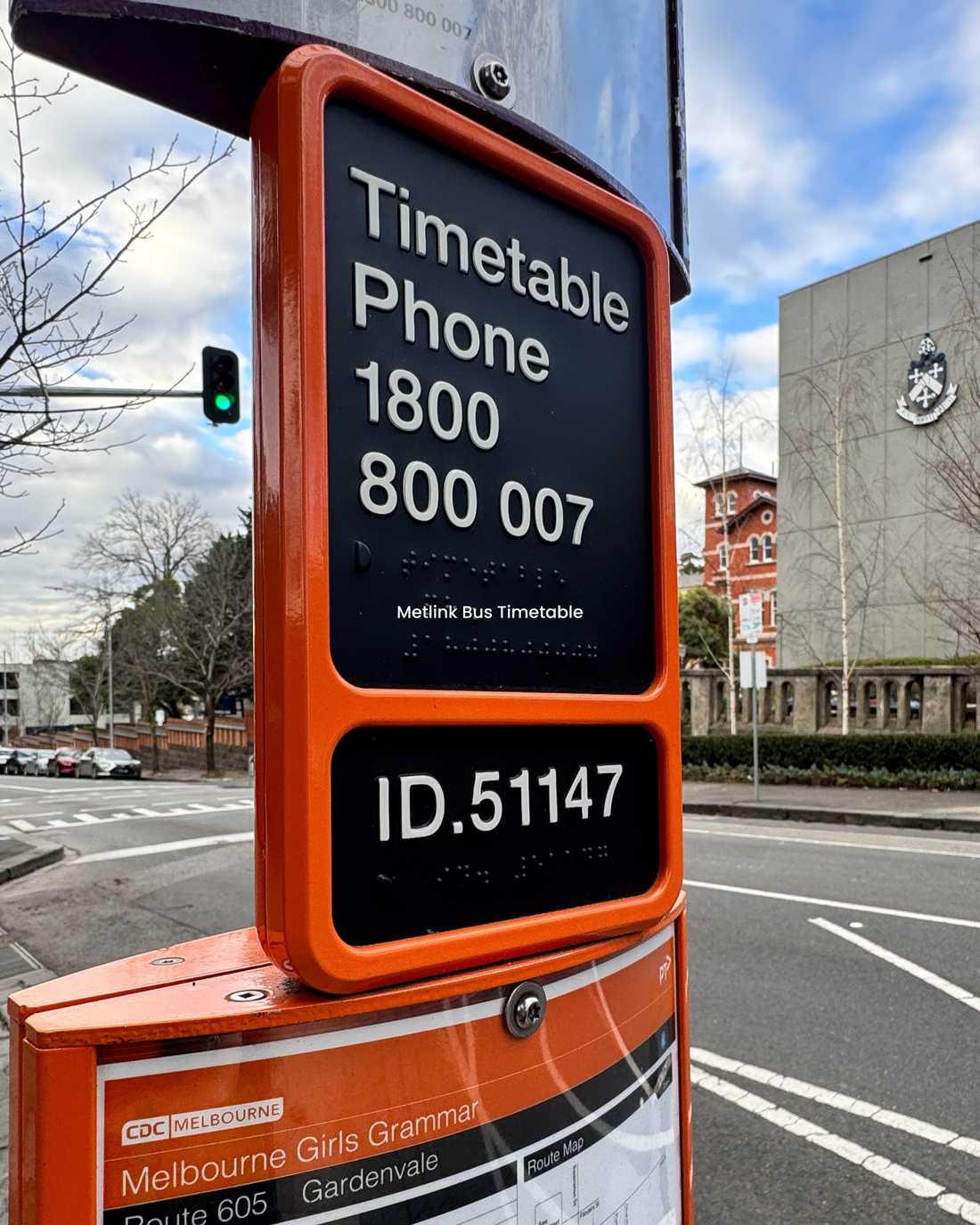 Black braille sign, with an orange border, of timetable phone number at a bus stop.